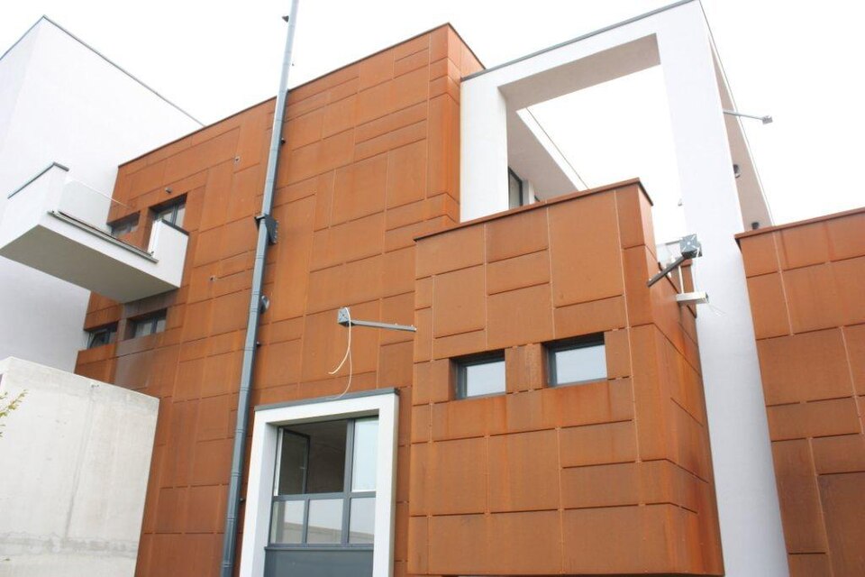 Closer upward architectural view of visibly fixed 3 mm Corten steel flat-sheet cladding. Same building as the orange facade candidate.